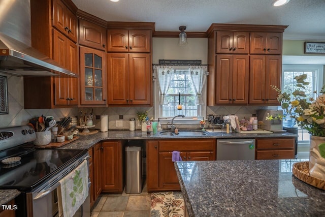 kitchen with a sink, stainless steel appliances, brown cabinets, and wall chimney range hood