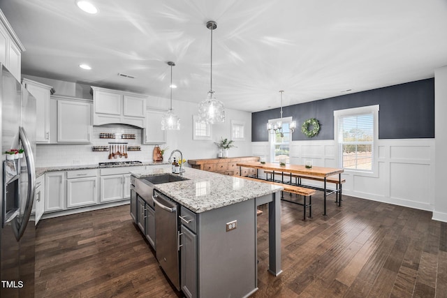 kitchen featuring dark wood-style floors, an island with sink, a sink, stainless steel appliances, and white cabinets