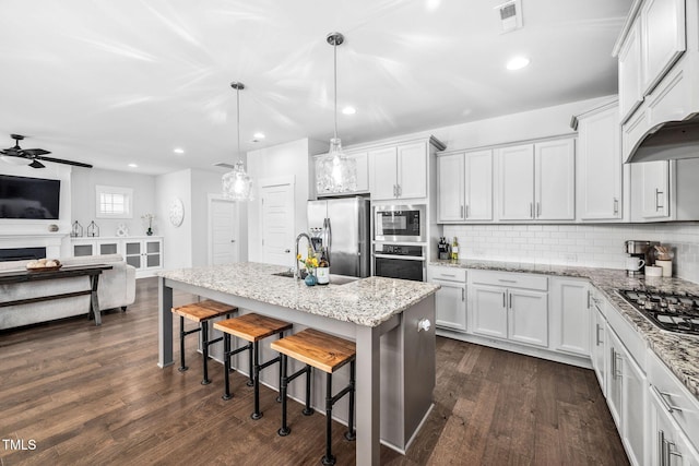 kitchen featuring visible vents, a kitchen breakfast bar, backsplash, dark wood finished floors, and stainless steel appliances