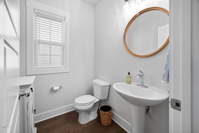 half bathroom with a sink, toilet, baseboards, and wood finished floors