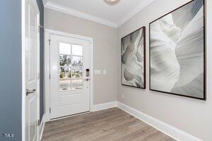 doorway featuring crown molding, baseboards, and wood finished floors