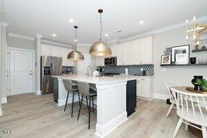 kitchen featuring light wood-style flooring, ornamental molding, stainless steel appliances, white cabinets, and pendant lighting