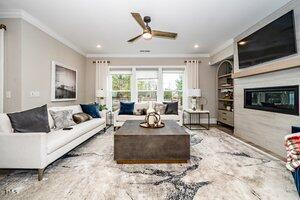 living room featuring built in features, ceiling fan, a glass covered fireplace, and ornamental molding