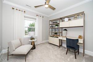 living area with baseboards, ceiling fan, ornamental molding, built in desk, and light colored carpet