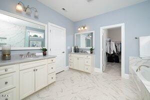 bathroom with baseboards, two vanities, a sink, a bath, and marble finish floor