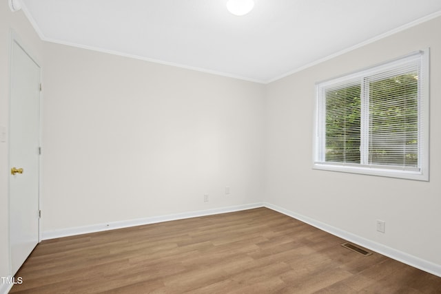 spare room with crown molding, baseboards, wood finished floors, and visible vents