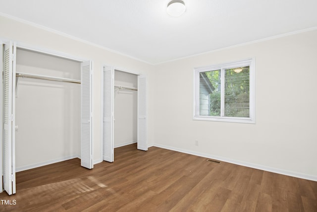 unfurnished bedroom featuring visible vents, ornamental molding, wood finished floors, two closets, and baseboards