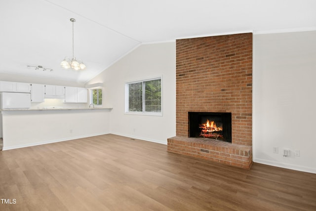 unfurnished living room featuring an inviting chandelier, wood finished floors, a fireplace, baseboards, and vaulted ceiling