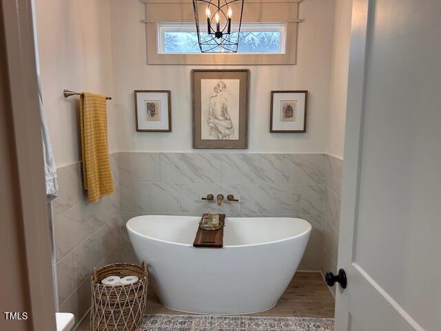 bathroom with a freestanding tub, tile walls, an inviting chandelier, and wainscoting