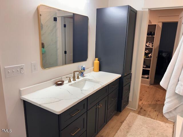 full bath featuring a spacious closet, a shower stall, vanity, and wood finished floors