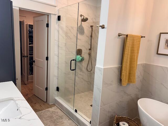 bathroom with a freestanding tub, a stall shower, wood finished floors, tile walls, and wainscoting