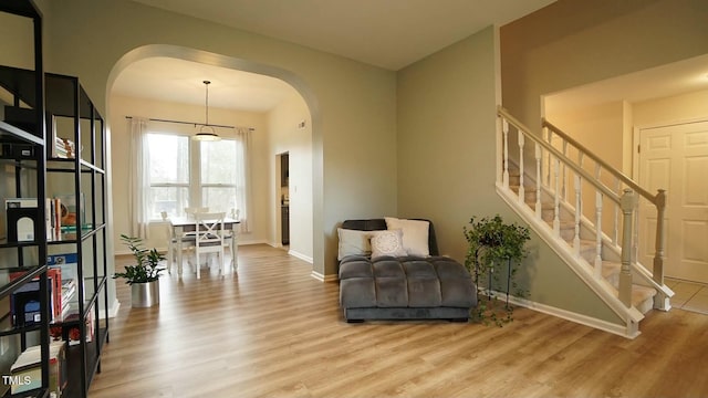 sitting room with stairs, wood finished floors, arched walkways, and baseboards