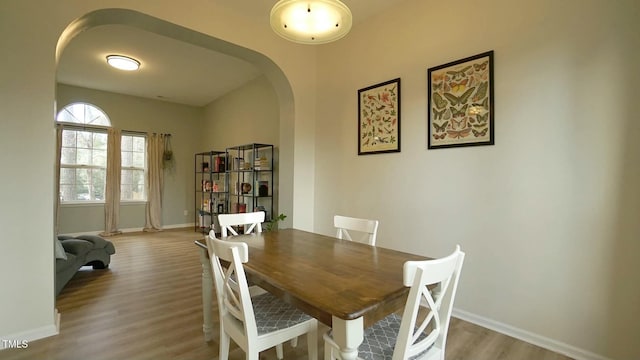 dining room with arched walkways, baseboards, and wood finished floors