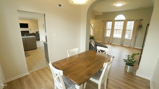 dining room with visible vents, light wood-style flooring, arched walkways, a fireplace, and baseboards