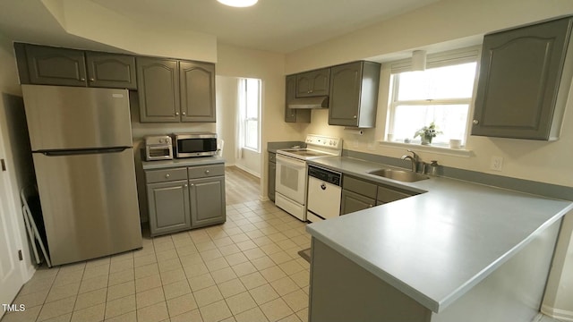 kitchen with light tile patterned floors, a peninsula, a sink, under cabinet range hood, and appliances with stainless steel finishes