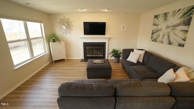 living room featuring baseboards, a fireplace with flush hearth, visible vents, and wood finished floors