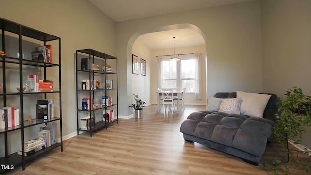 living area featuring wood finished floors, arched walkways, and baseboards