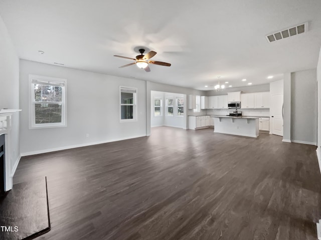 unfurnished living room with visible vents, baseboards, a fireplace with flush hearth, and dark wood-style flooring