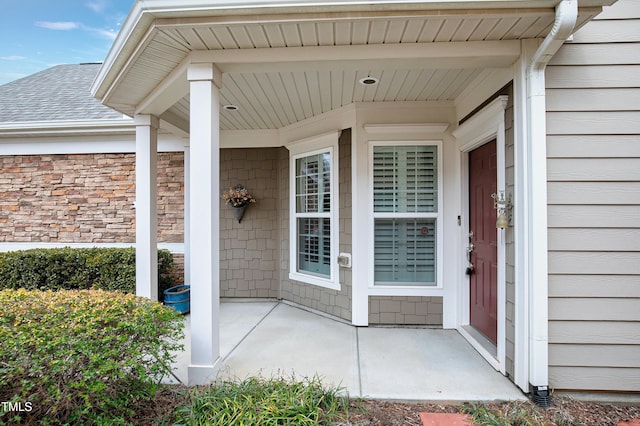 property entrance with covered porch and a shingled roof