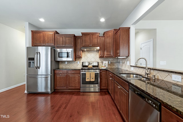 kitchen featuring dark wood-type flooring, a sink, under cabinet range hood, dark stone countertops, and stainless steel appliances