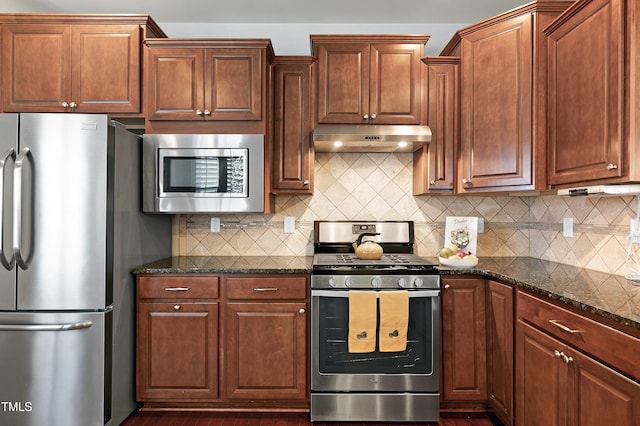 kitchen featuring under cabinet range hood, backsplash, appliances with stainless steel finishes, and dark stone countertops