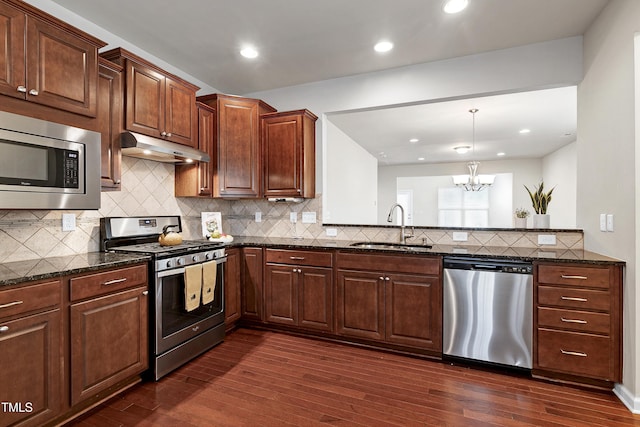 kitchen featuring a sink, under cabinet range hood, dark stone countertops, stainless steel appliances, and dark wood-style flooring