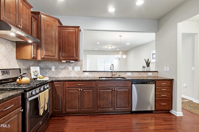 kitchen with a sink, under cabinet range hood, stainless steel appliances, dark stone counters, and dark wood-style flooring