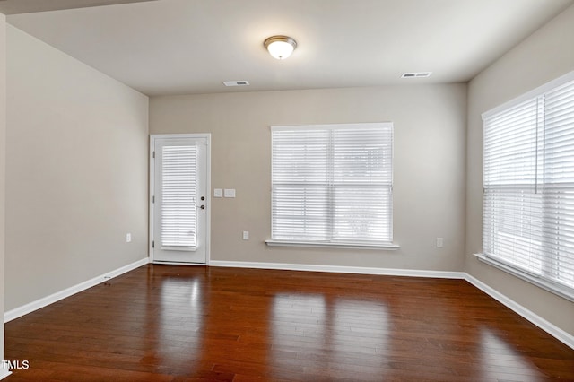 empty room featuring dark wood-style floors, visible vents, and baseboards