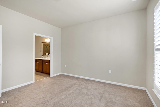 unfurnished bedroom featuring light carpet, ensuite bathroom, baseboards, and a sink