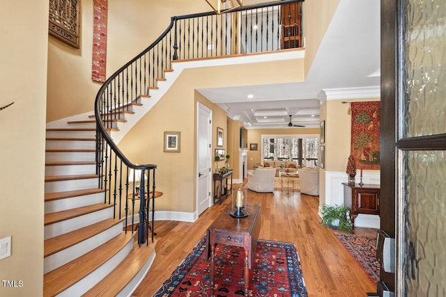 entrance foyer featuring coffered ceiling, wood finished floors, a high ceiling, and ornamental molding