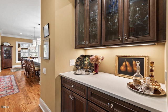 bar featuring hanging light fixtures, crown molding, baseboards, and light wood finished floors