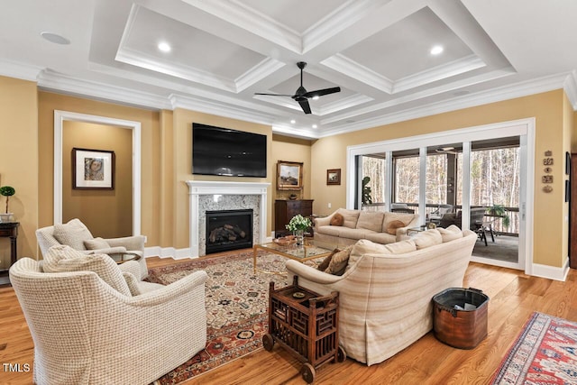 living area featuring ornamental molding, a ceiling fan, coffered ceiling, a fireplace, and light wood finished floors