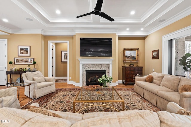 living area with a high end fireplace, crown molding, a raised ceiling, and wood finished floors