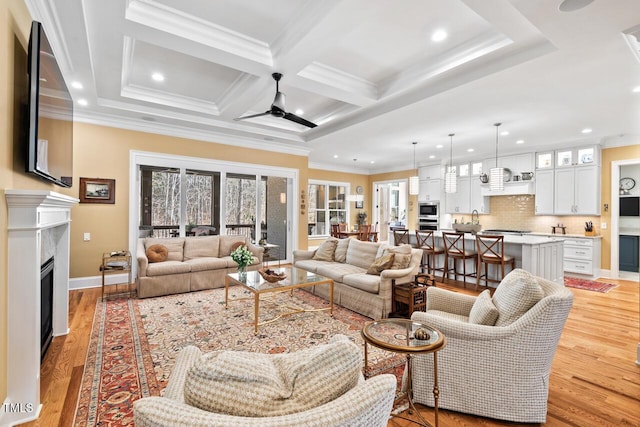 living room with light wood finished floors, ornamental molding, a fireplace, coffered ceiling, and a ceiling fan