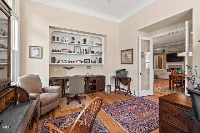 office area with wood finished floors, baseboards, a fireplace, ceiling fan, and ornamental molding