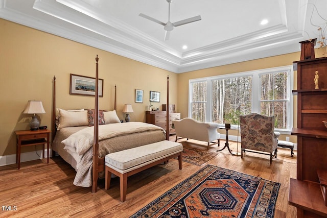 bedroom featuring a tray ceiling, recessed lighting, light wood-style floors, crown molding, and baseboards