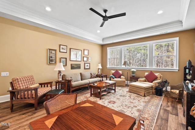 living room featuring ceiling fan, a raised ceiling, wood finished floors, and ornamental molding