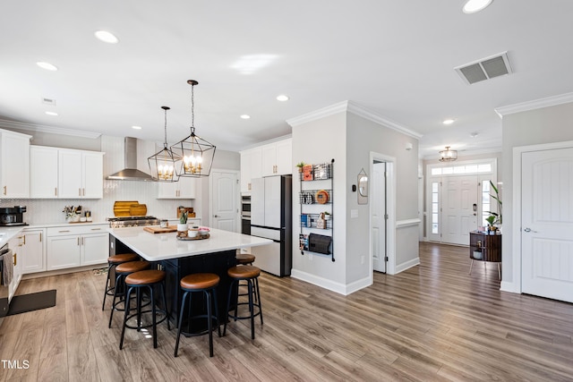 kitchen featuring crown molding, wall chimney range hood, visible vents, and freestanding refrigerator