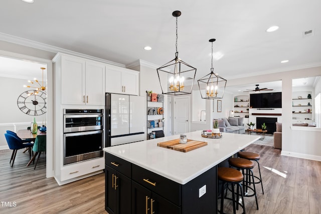 kitchen featuring dark cabinetry, a kitchen island, freestanding refrigerator, light wood-style floors, and crown molding