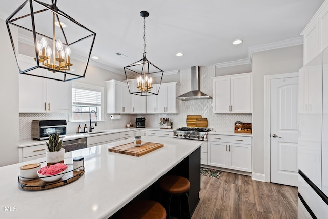 kitchen featuring a notable chandelier, a sink, wall chimney range hood, crown molding, and light countertops