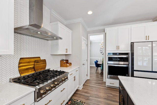 kitchen with wood finished floors, ornamental molding, stainless steel appliances, white cabinetry, and wall chimney exhaust hood