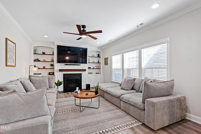 living area with built in shelves, wood finished floors, visible vents, a fireplace, and ornamental molding