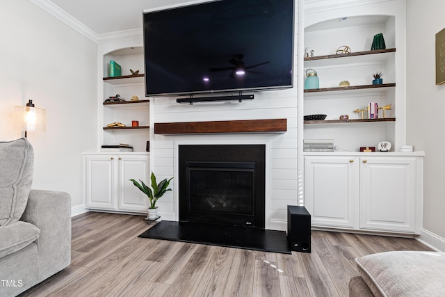 living room with built in shelves, ornamental molding, a large fireplace, light wood-style floors, and baseboards