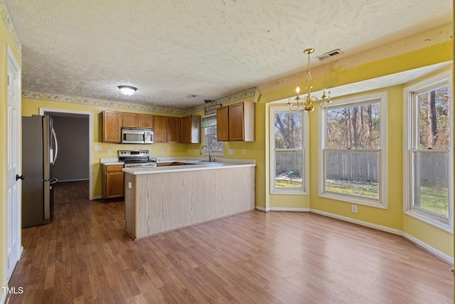 kitchen with brown cabinetry, visible vents, dark wood finished floors, a peninsula, and stainless steel appliances