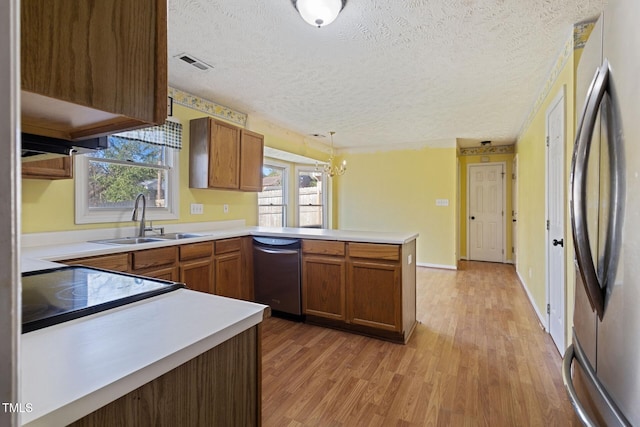 kitchen featuring visible vents, a peninsula, light wood-style flooring, a sink, and stainless steel appliances