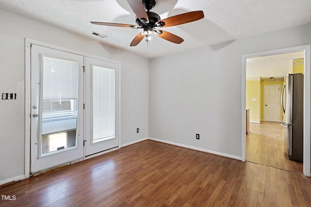 spare room featuring visible vents, baseboards, a textured ceiling, and wood finished floors