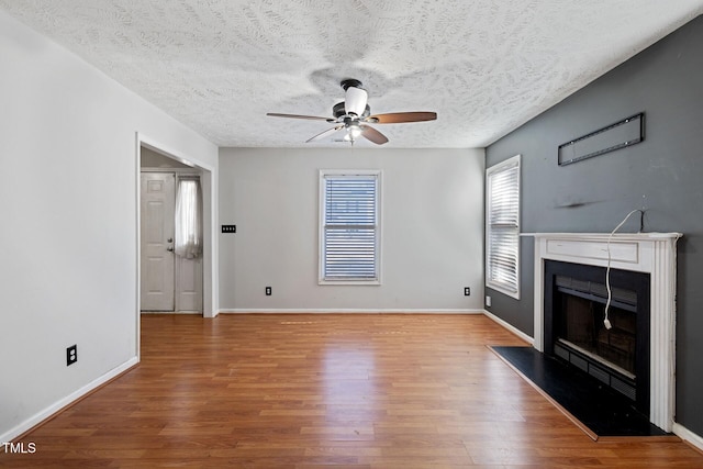 unfurnished living room with ceiling fan, baseboards, wood finished floors, and a fireplace