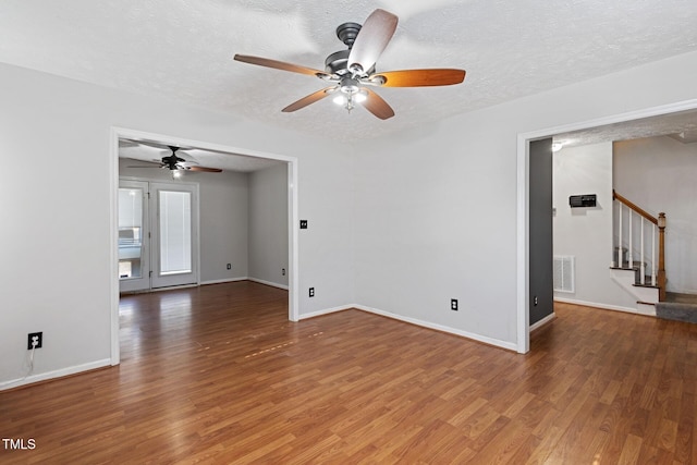 unfurnished living room featuring visible vents, stairway, a textured ceiling, and wood finished floors