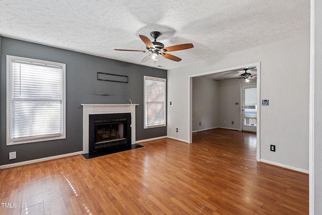 unfurnished living room with a ceiling fan, a fireplace with flush hearth, wood finished floors, and baseboards