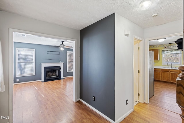 hallway with a textured ceiling, light wood-type flooring, baseboards, and a sink